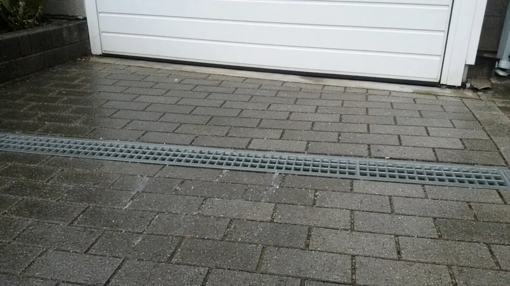 Linear channel drain across a block paved drive in front of a garage