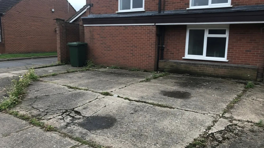 Old concrete driveway cracked across the middle with weeds in the joints